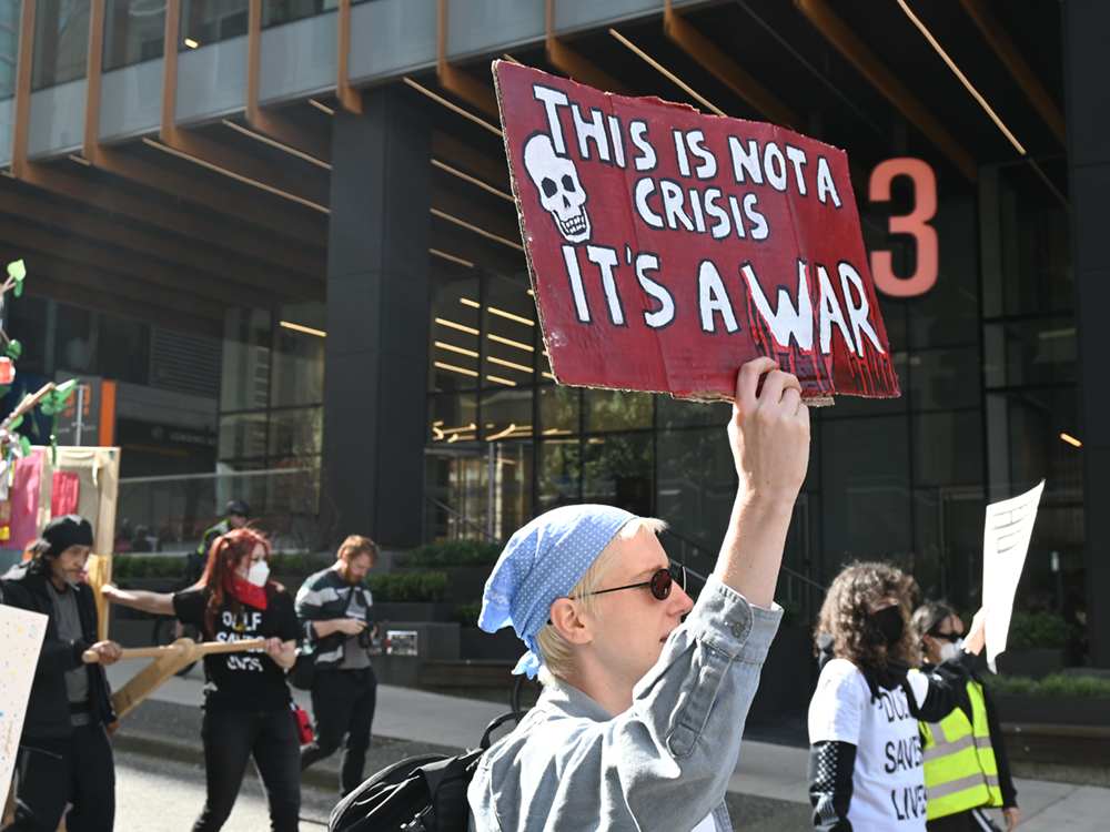 A person holds up a sign reading, 'This is not a crisis, it’s a war.'
