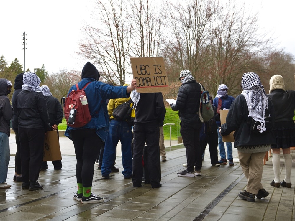 Students wear kaffiyehs and cover their faces. One student holds a sign reading, ‘UBC is complicit.’