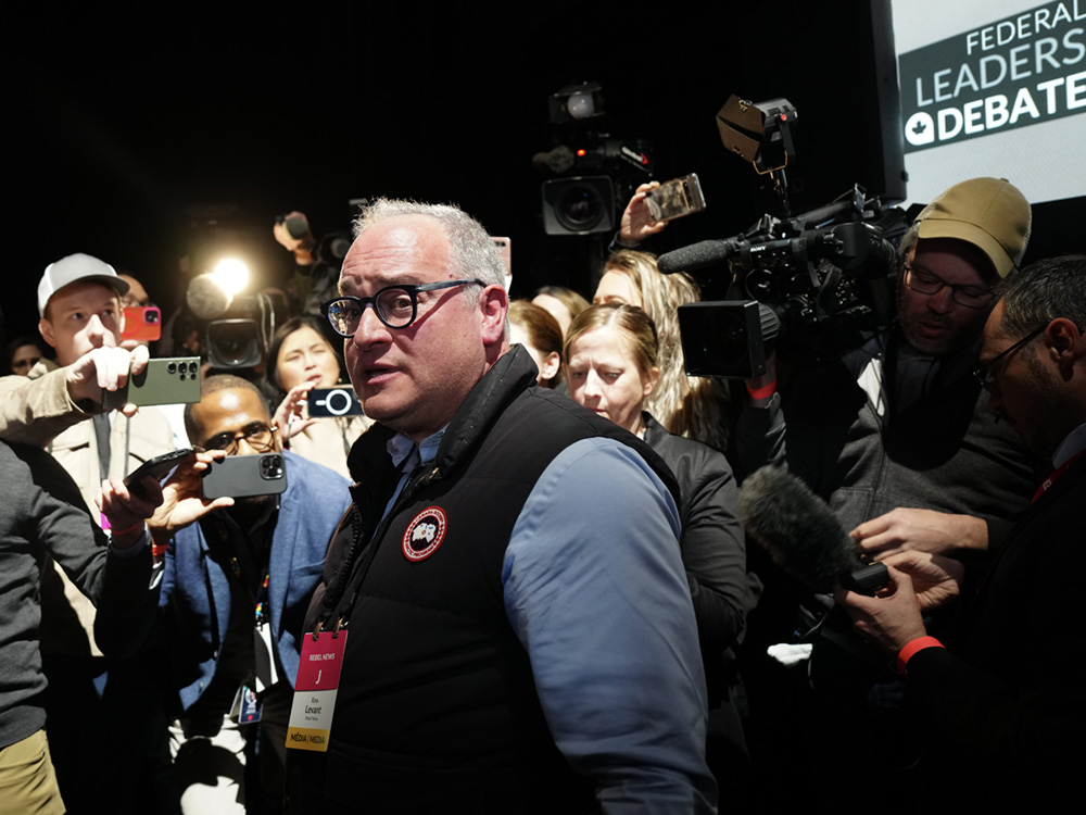 Ezra Levant stands in the foreground, surrounded by a ton of journalists and photographers taking photos and video.