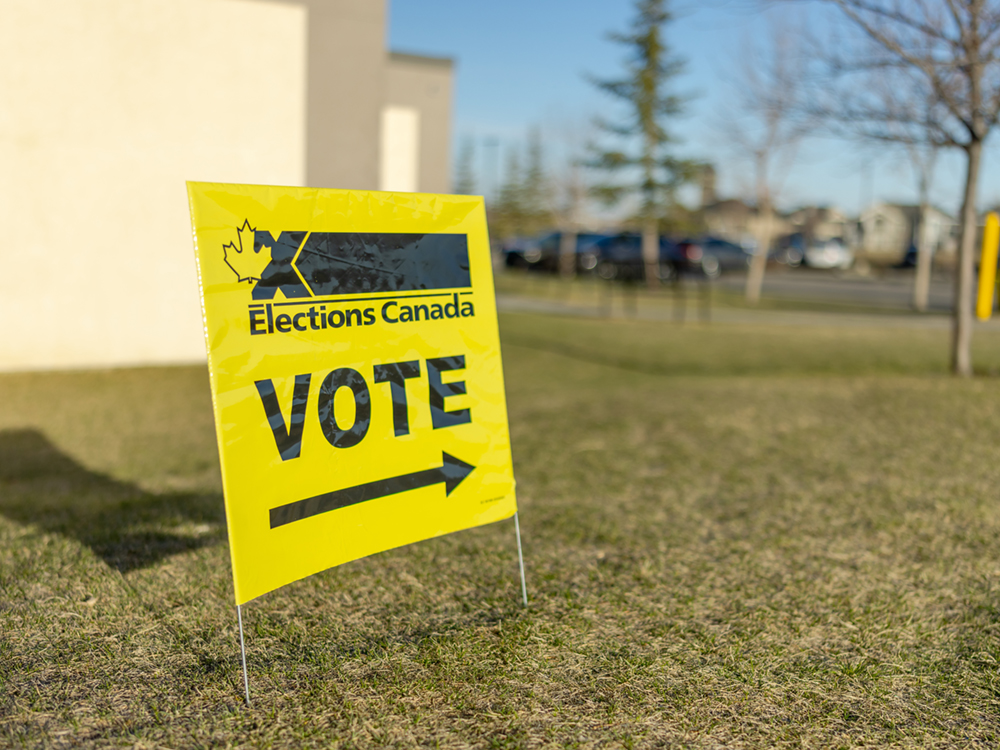 A yellow sign reads, ‘Elections Canada’ and ‘VOTE,’ with an arrow pointing towards the polling place.