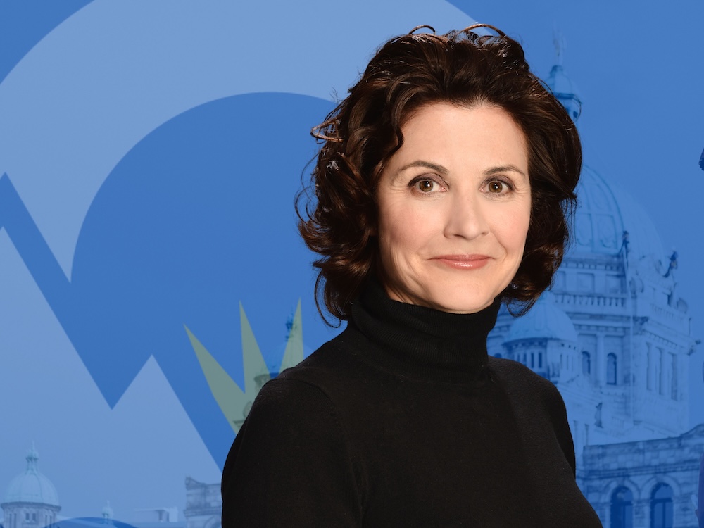 A middle-aged, light-skinned woman with black hair and wearing a black shirt poses.