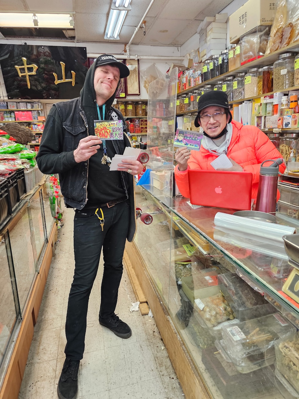 Trey Helten poses with postcards of graffiti with a shop owner in Chinatown. 
