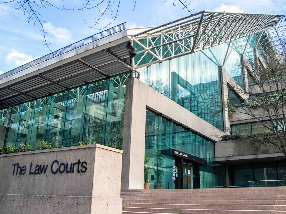 A grey concrete building features stairs and a slanted glass atrium. The words ‘The Law Courts’ are visible on the concrete wall to the left of the frame and above a door. It’s a clear winter day and the sky is blue.