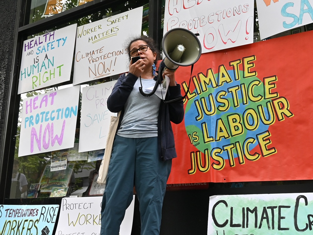 Ingrid Mendez, a woman with medium-light skin tone, glasses and dark hair, gives a speech outside David Eby&rsquo;s MLA office.