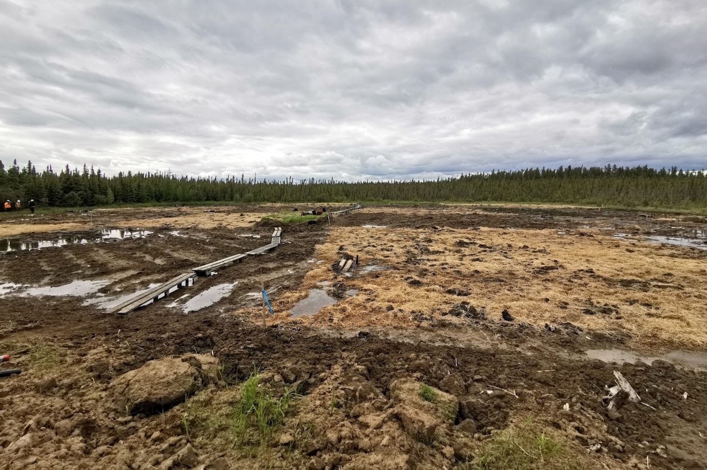 A barren well pad site covered in dirt, mud and brown grass.