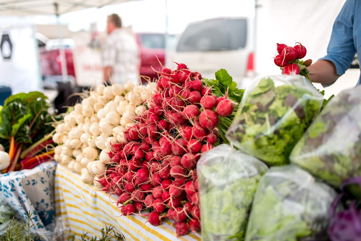 A table is piled high with white turnips, red radishes and bagged green lettuce. 