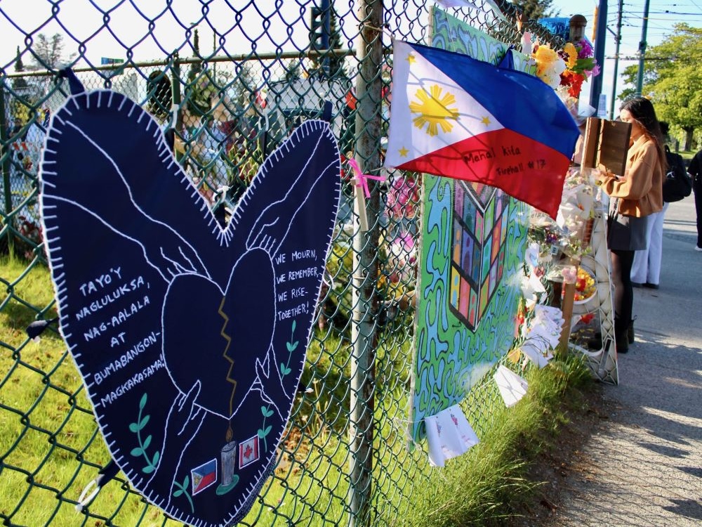 A chain-link fence outside a grassy area holds signs, flags and notes.