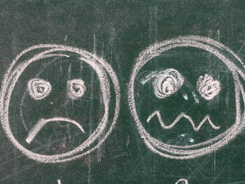 Simple chalked faces on a blackboard, one frowning, the other with a wiggled line mouth showing frustration.