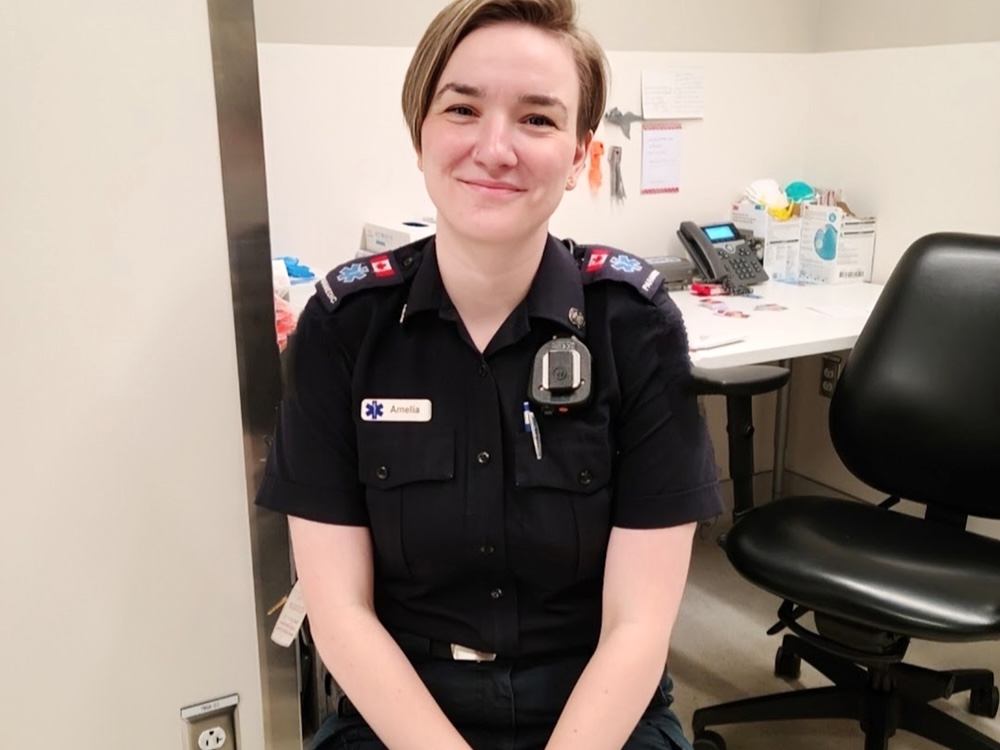 Amelia Bridge wears a paramedic uniform. She is a young woman with light skin tone and short light brown hair.