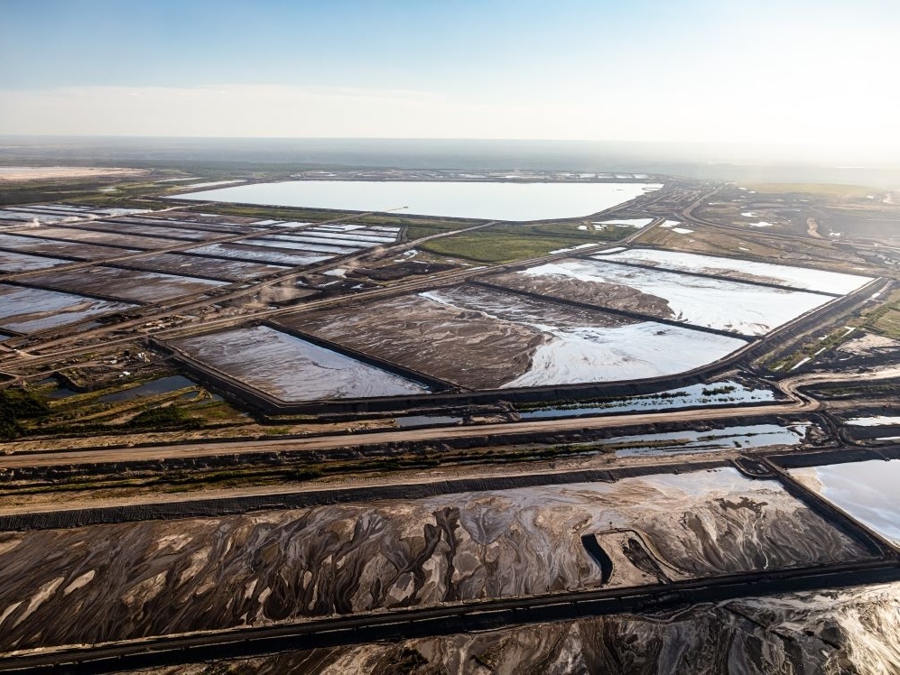 An aerial shot shows vast tailings ponds, some full of water and others sludge.