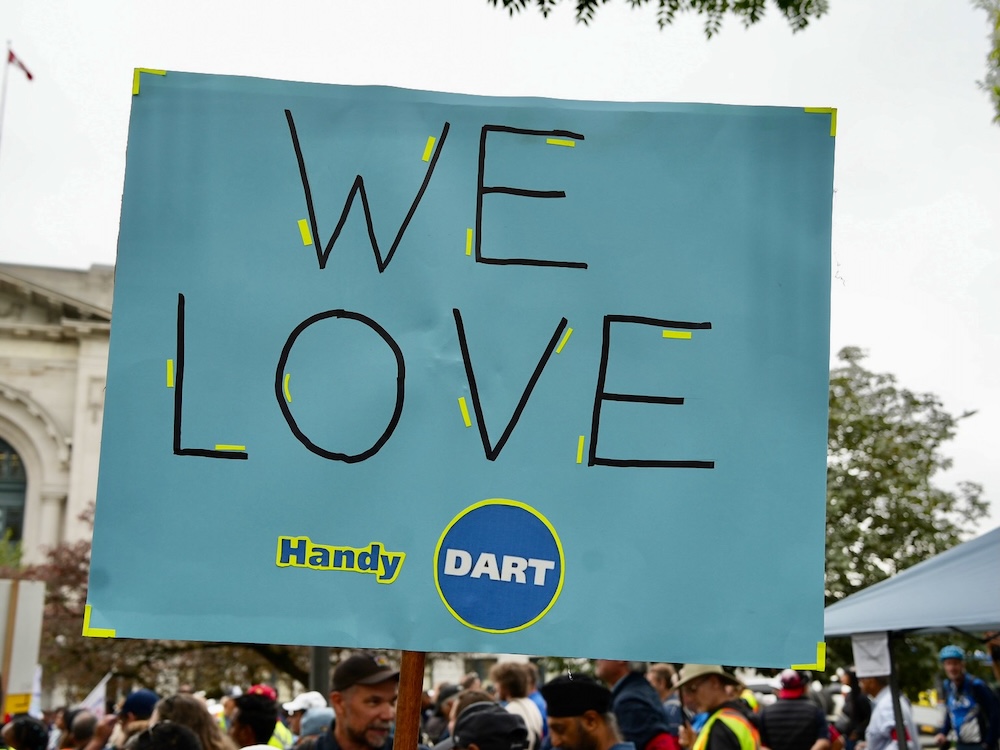 A protest sign at a gathering in downtown Vancouver reads, ‘We love HandyDart.’