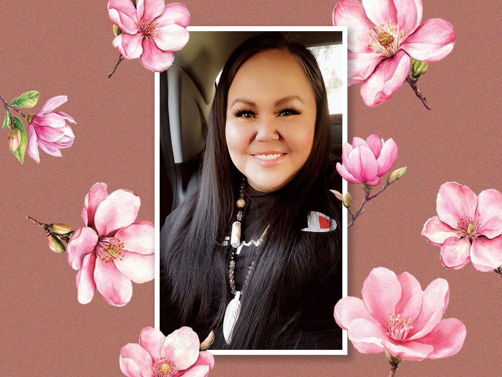 Melanie Lecoy has long dark hair and a medium skin tone. She is smiling at the camera and seated in a car. She is wearing a black jacket and a large beaded necklace with a white feather pendant. Her photograph is surrounded by a white border and set against a terra cotta background across which large pink flowers are blooming.