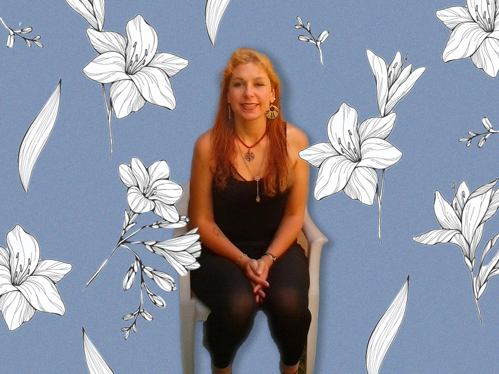 A young woman with long reddish-blond hair smiles at the camera, seated in a white chair. She wears a necklace and a black top and slacks. Her photo is superimposed on a purple background with white flowers.