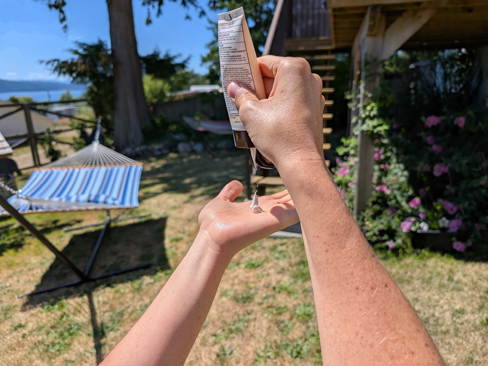 A person with freckly arms squeezes a sunscreen tube. Sunscreen drops into their open palm.