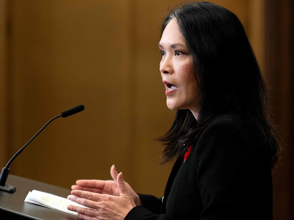 Jenny Kwan, a 58-year-old woman of Chinese descent, speaks while standing at a lectern.