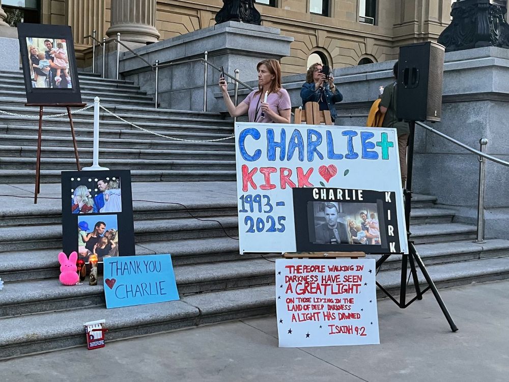 Signs, photos and flowers are in front of the sandstone Alberta legislature.