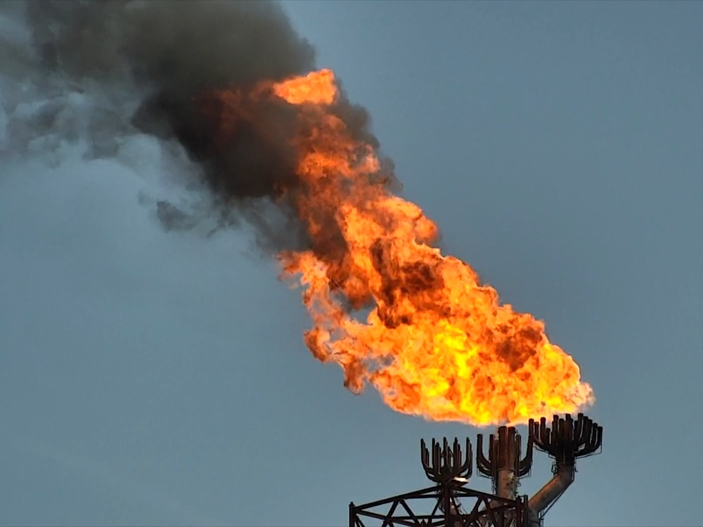 A large LNG flare with bright orange fire and a dark sooty cloud.
