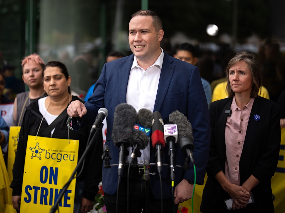 Paul Finch, a 40-ish light-skinned man with short hair, stands in front of a bank of microphones.