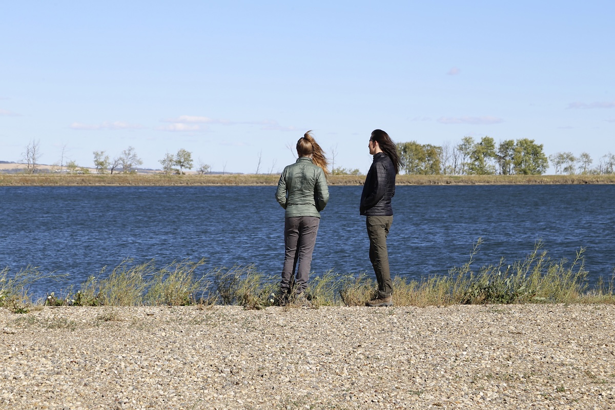 Two women stand with their backs to the camera. In front of them is a water reservoir.
