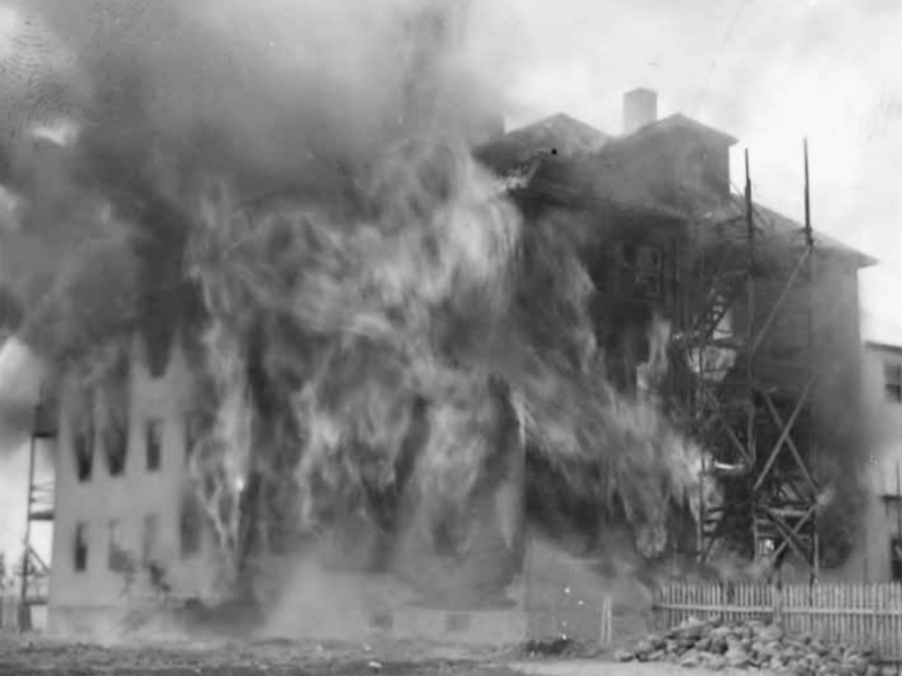 Flames tear through a three-storey building in a black and white photo.