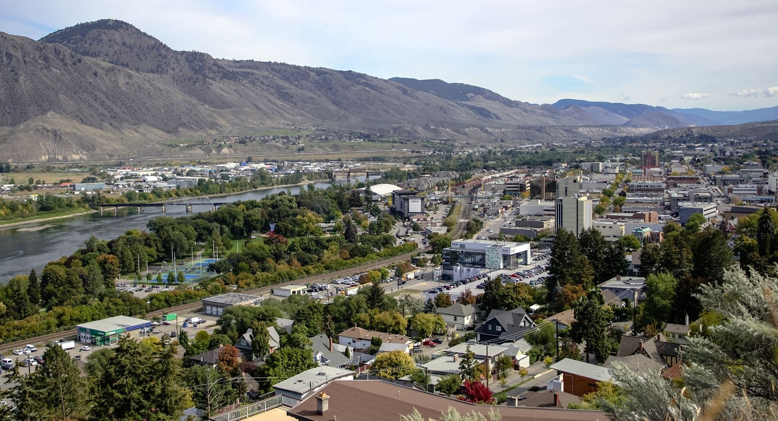 Aerial view of a mid-sized city on the banks of a river, backed by hills.