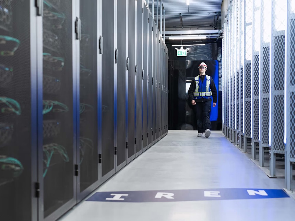 A man wearing a blue work suit walks down a hallway lined with technical equipment.