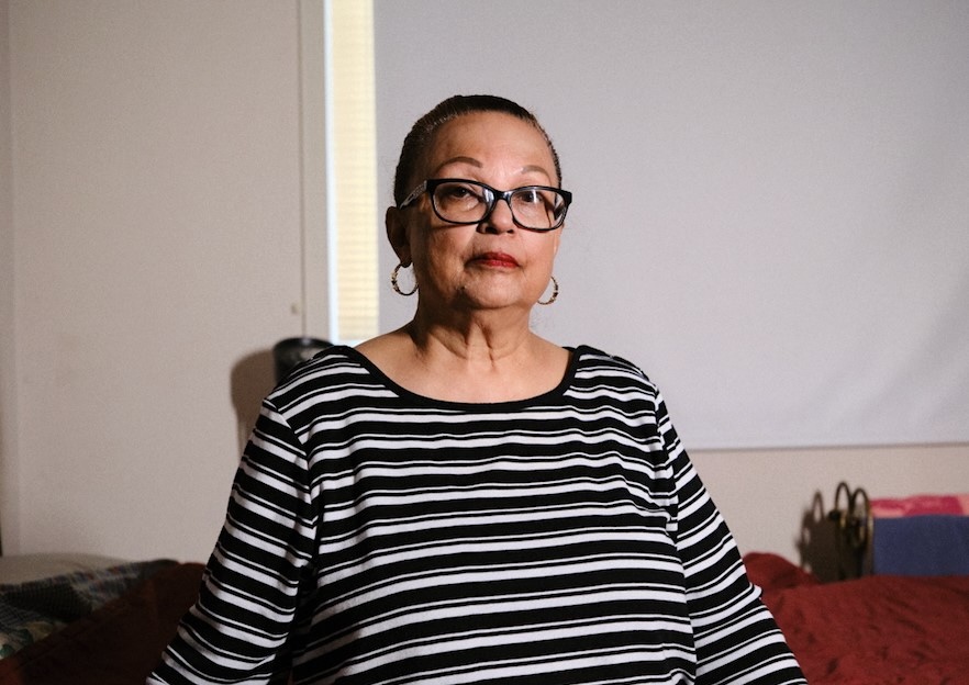 A woman in her 70s, wearing glasses and a black and white striped sweater. 