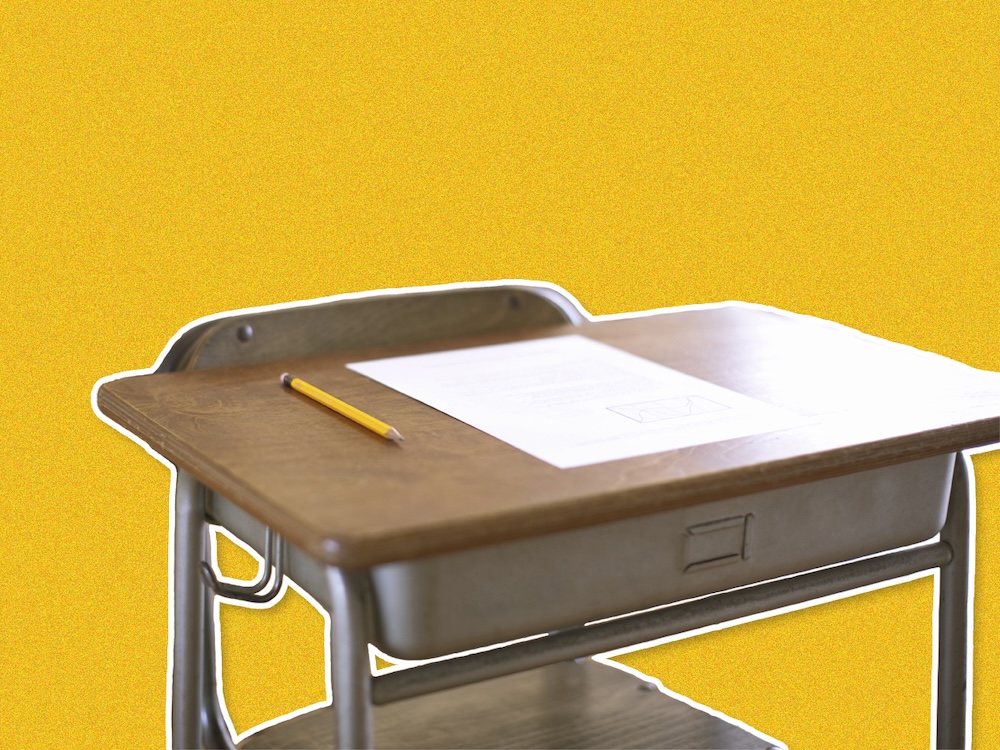 An empty desk with a test on top, on a yellow background.