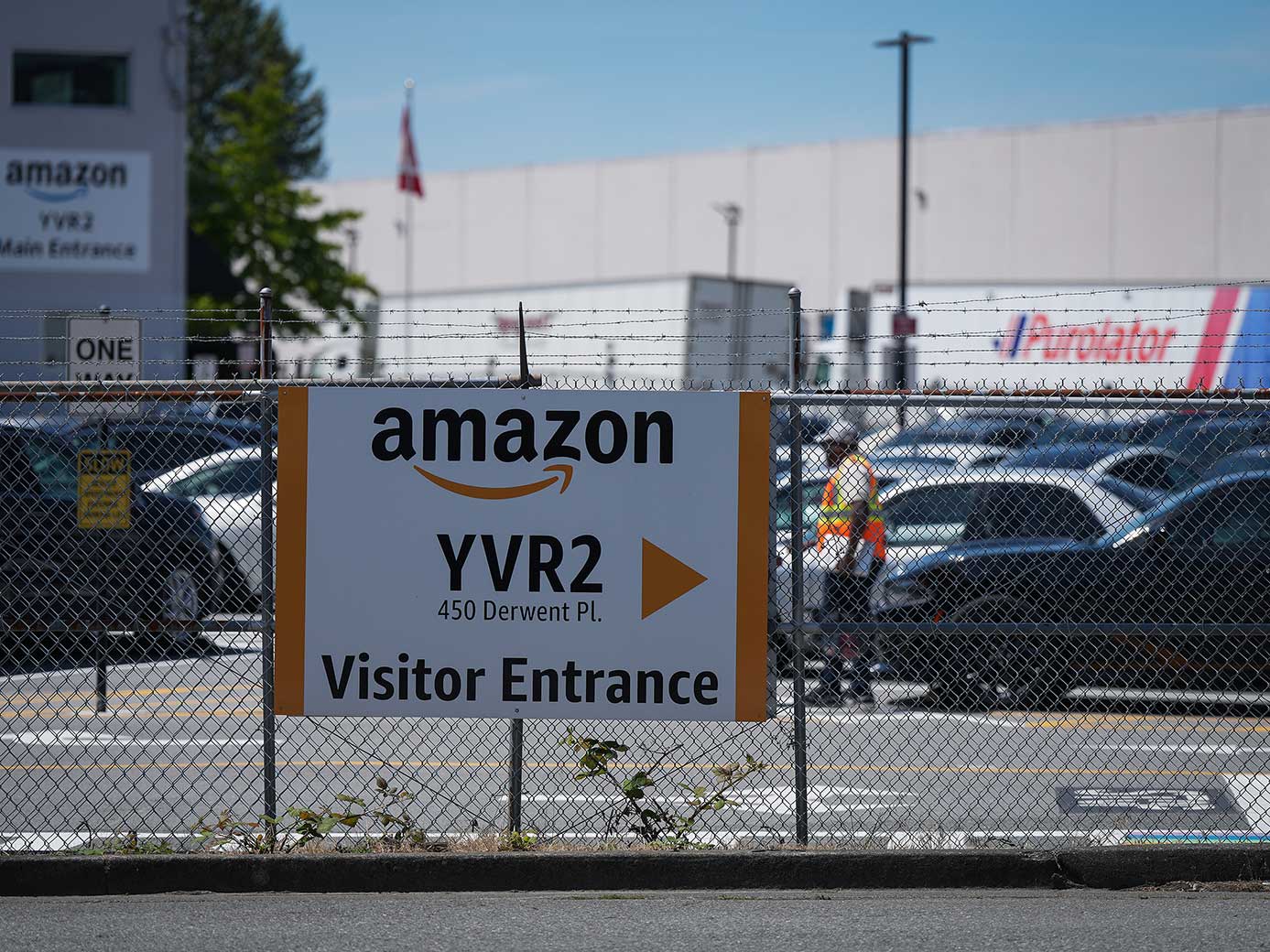 A sign that reads &ldquo;amazon YVR2&rdquo; in front of a large white warehouse building.