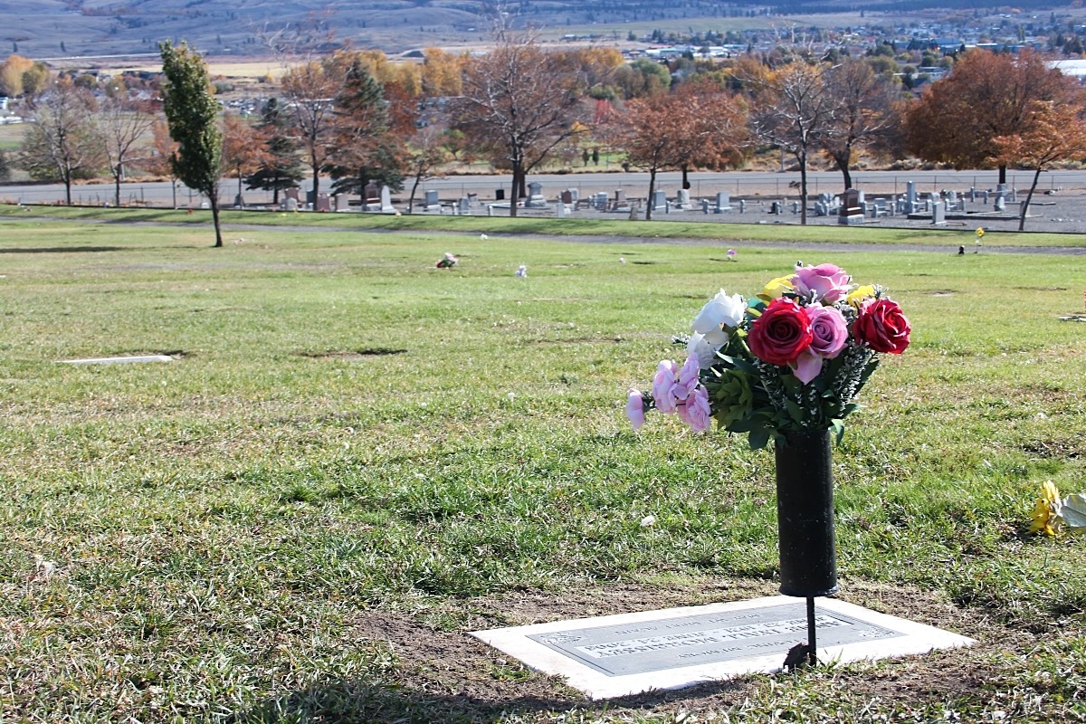 A large grassy area is home to spaced-out grave markers. It&rsquo;s on a sloping hillside.