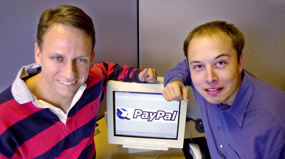 Two young men with light skin and brown hair on either side of an old-model computer screen displaying a &lsquo;PayPal&rsquo; logo.
