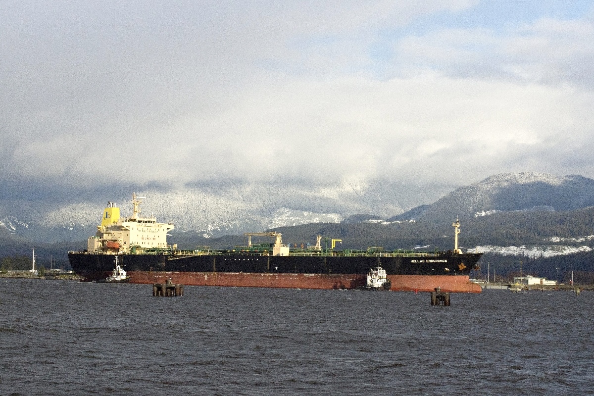A large oil tanker sits in harbour. Cloudy mountaintops loom over the tanker and the sea.