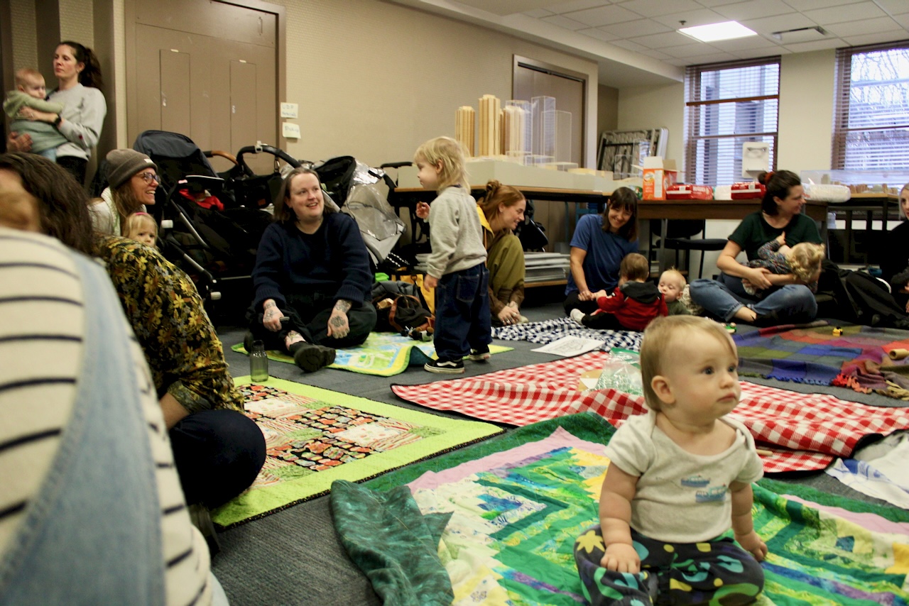 Babies crawl around on blankets while their parents watch in a meeting room at Vancouver City Hall.