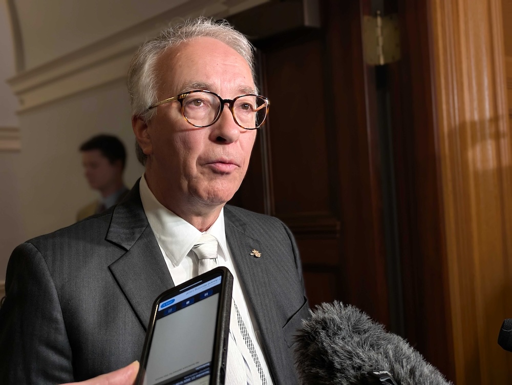 John Rustad, a mid-60s light-skinned man with grey hair, is being scrummed by reporters.