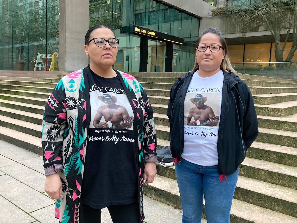 Two women stand in front of the steps of the Vancouver Supreme Court building. They wear white T-shirts with a photo of a man wearing a cowboy hat and no shirt. The shirts state the name of their relative, Jeff Caron, and the dates of his birth and death.