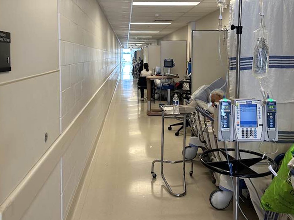 Beds are lined up in a hospital hallway. There are privacy curtains, IVs and other hospital items.