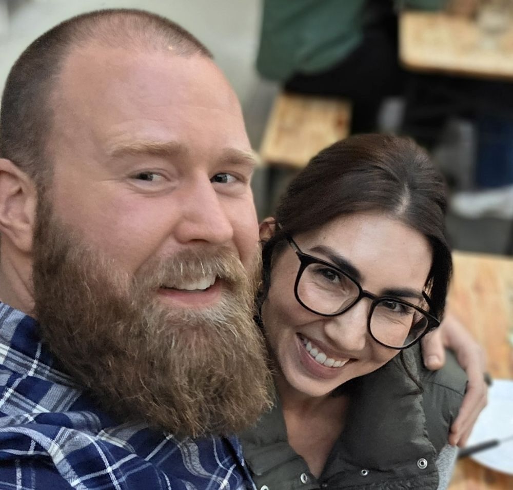 A man and a woman, both with light skin tone and brown hair, embrace each other and pose for a photo at a restaurant.