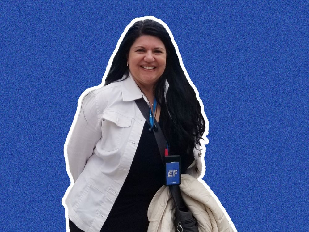 A woman with dark hair and light skin tone wears a white jacket and black shirt.