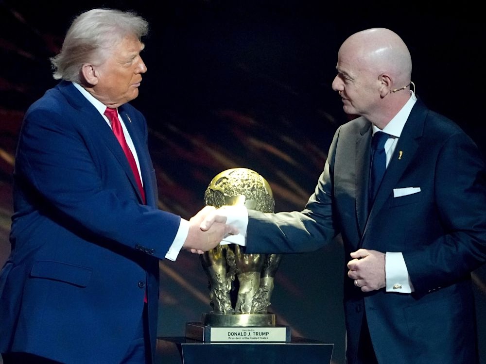 U.S. President Donald Trump shakes hands with a stylish light-skinned man with a shaved head. Between them is a large gold trophy.