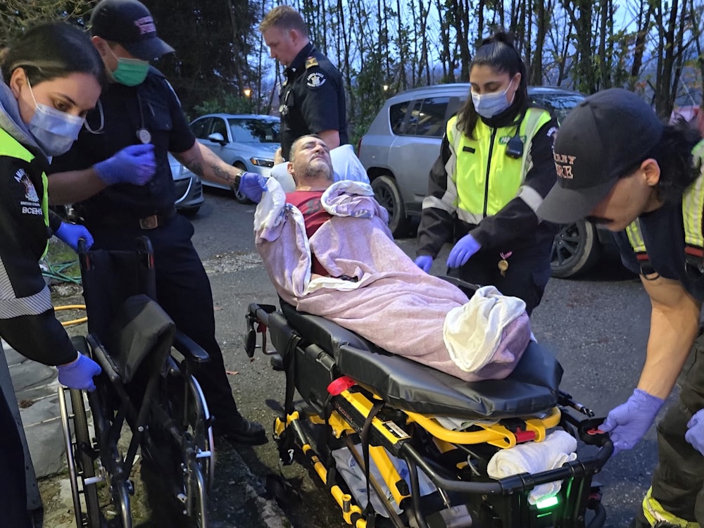 Paramedics are at work as a man lies on a stretcher looking exhausted, partly covered with a blanket.