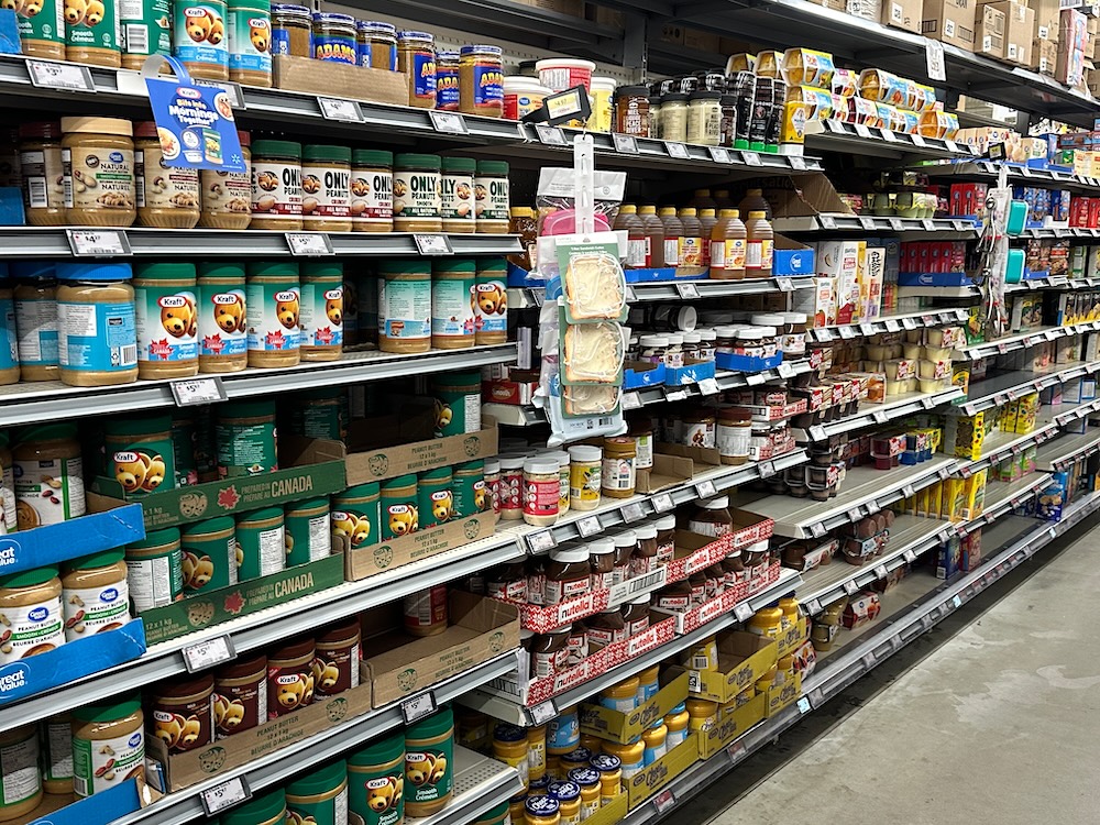 A grocery store shelf stocked with peanut butter and other items.