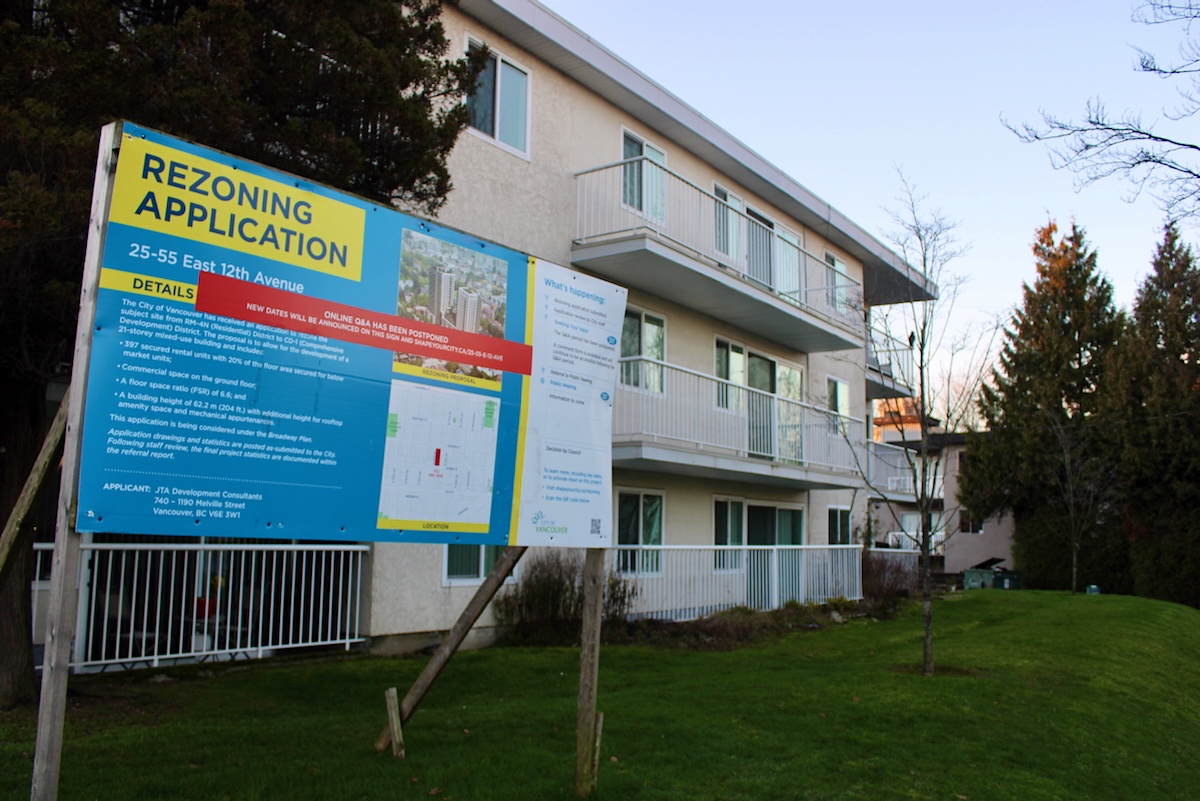 A white three-storey apartment building in Vancouver with a redevelopment sign in front.