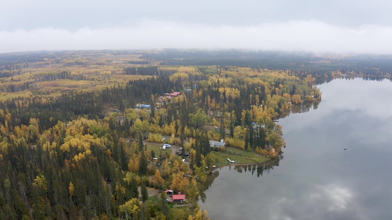An aerial image shows a rural community surrounded by forest beside a lake. 