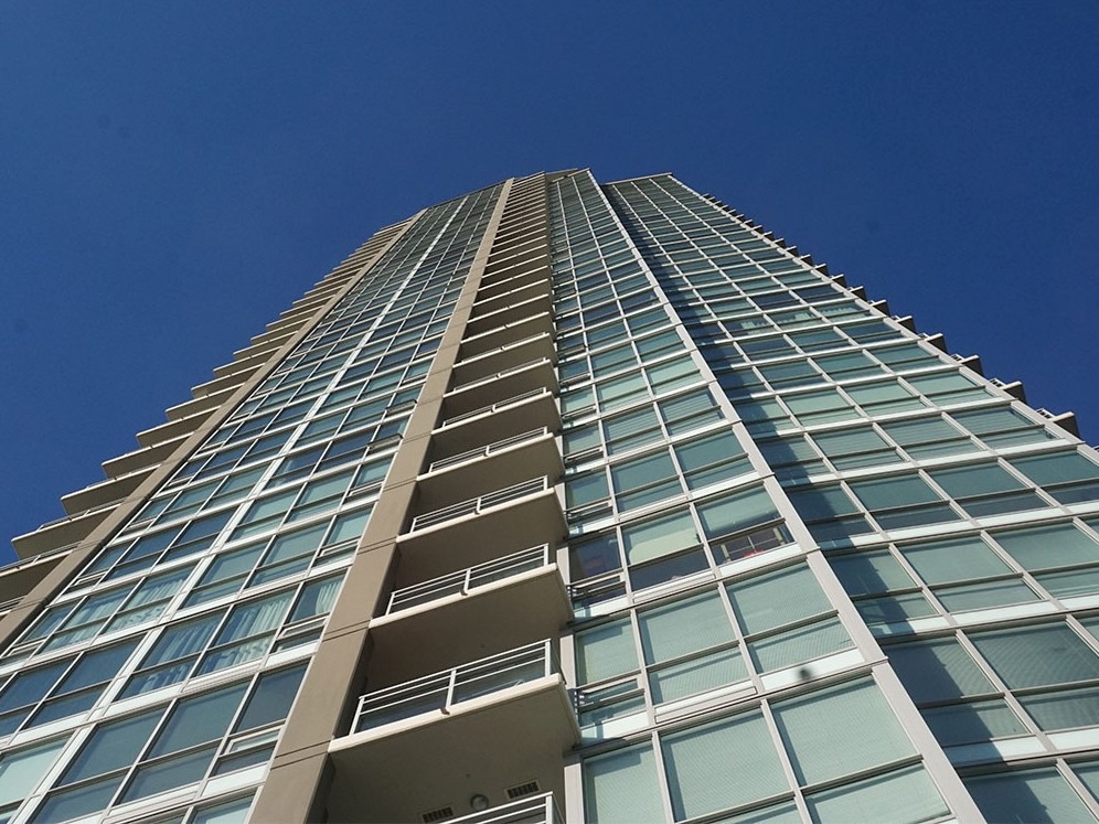 Seen from the bottom, a glass condo tower extends upwards towards a blue sky.