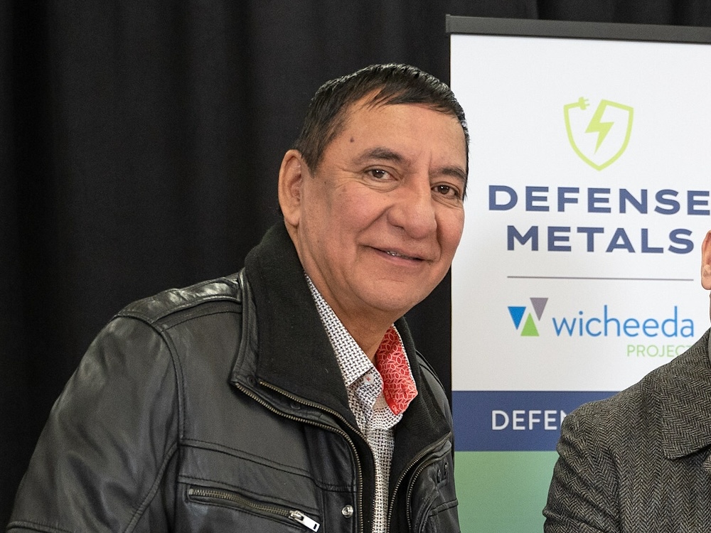 A First Nations man wearing a leather jacket poses for a photo alongside another unidentifiable person.