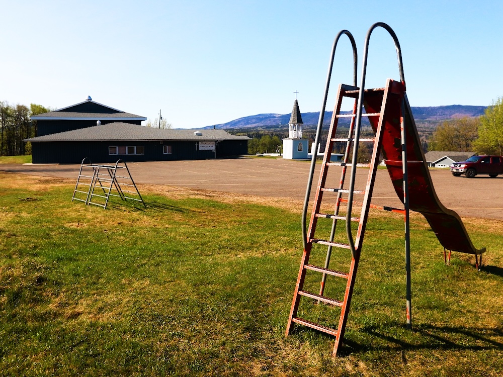 A metal slide sits unused a distance from a low-slung brown school building.