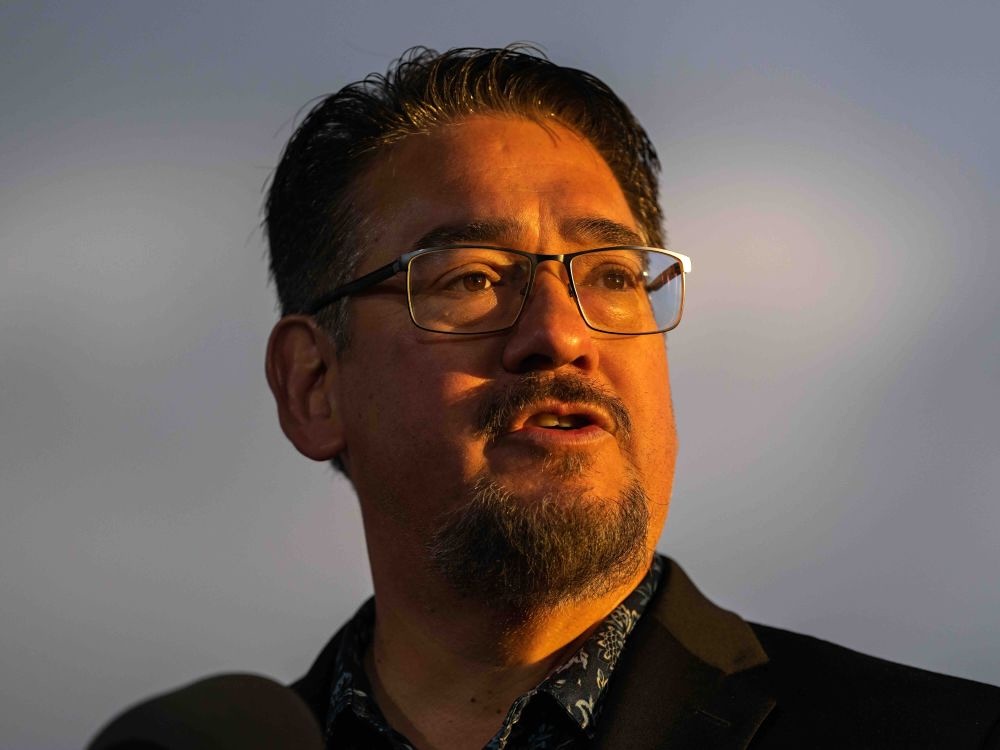 A 50-ish Indigenous man with a beard and glasses is bathed in a golden light.