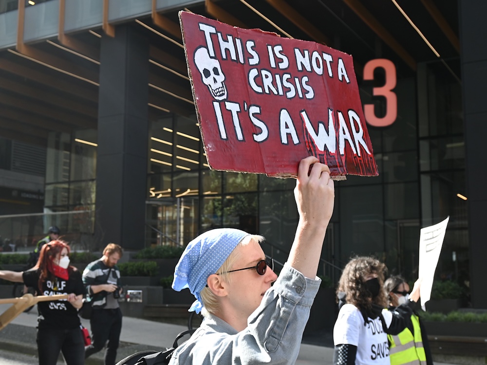 A person holds up a sign that reads, &lsquo;This is not a crisis. It&rsquo;s a war.&rsquo;
