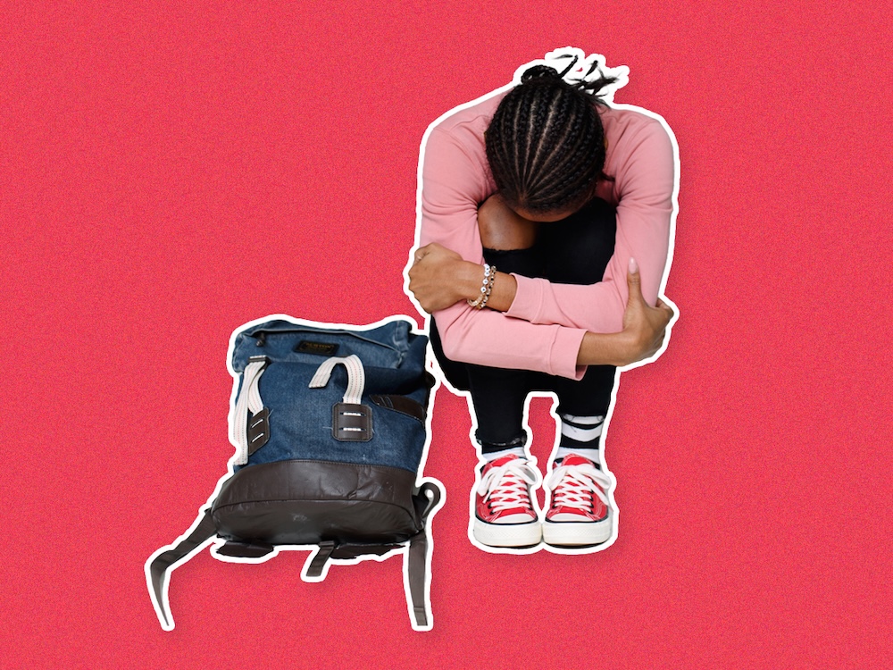 A young girl with medium-dark skin tone, and dark hair in cornrows, sits with her head in her lap and her arms around her knees. A backpack is on the ground in front of her.