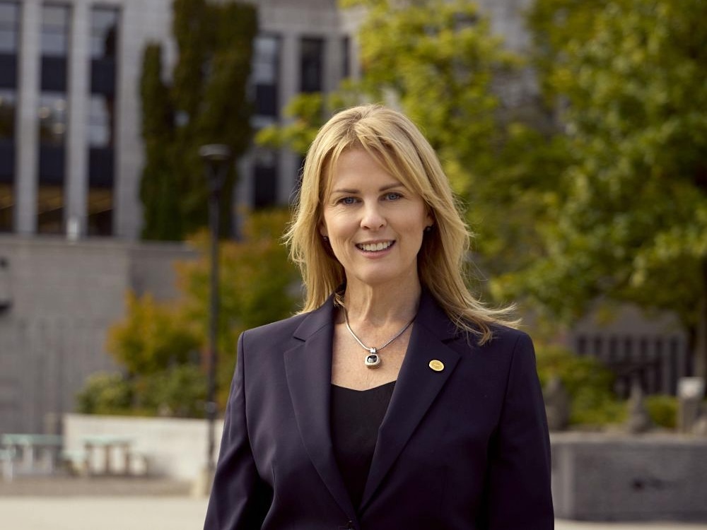 A woman with shoulder-length blond hair and bangs wears a black suit and smiles in a photo taken outside Vancouver City Hall.